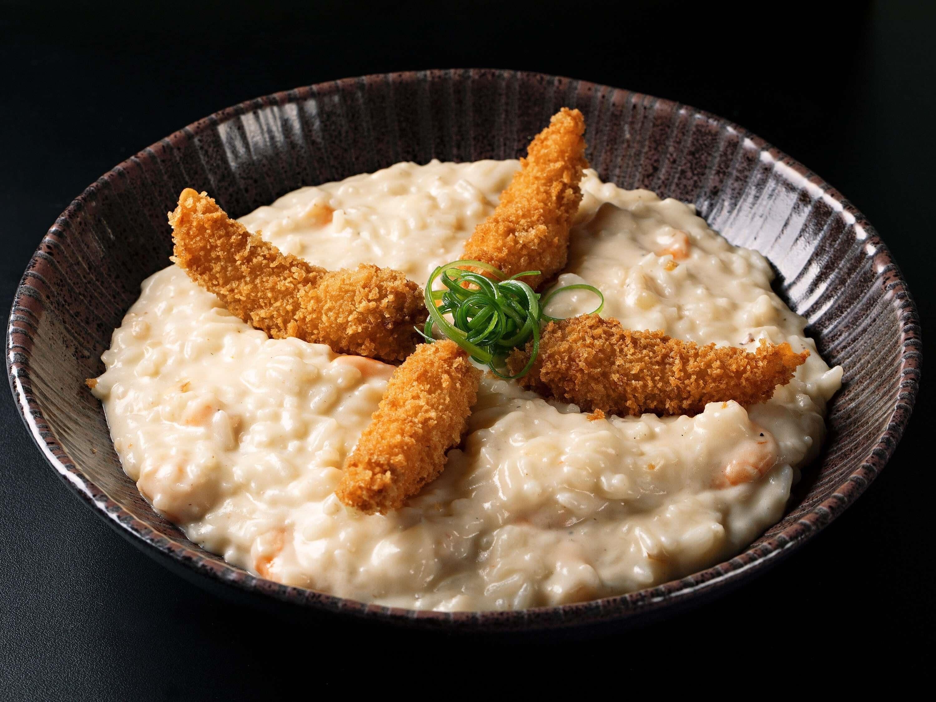 A bowl of creamy food with breaded items and green garnish.