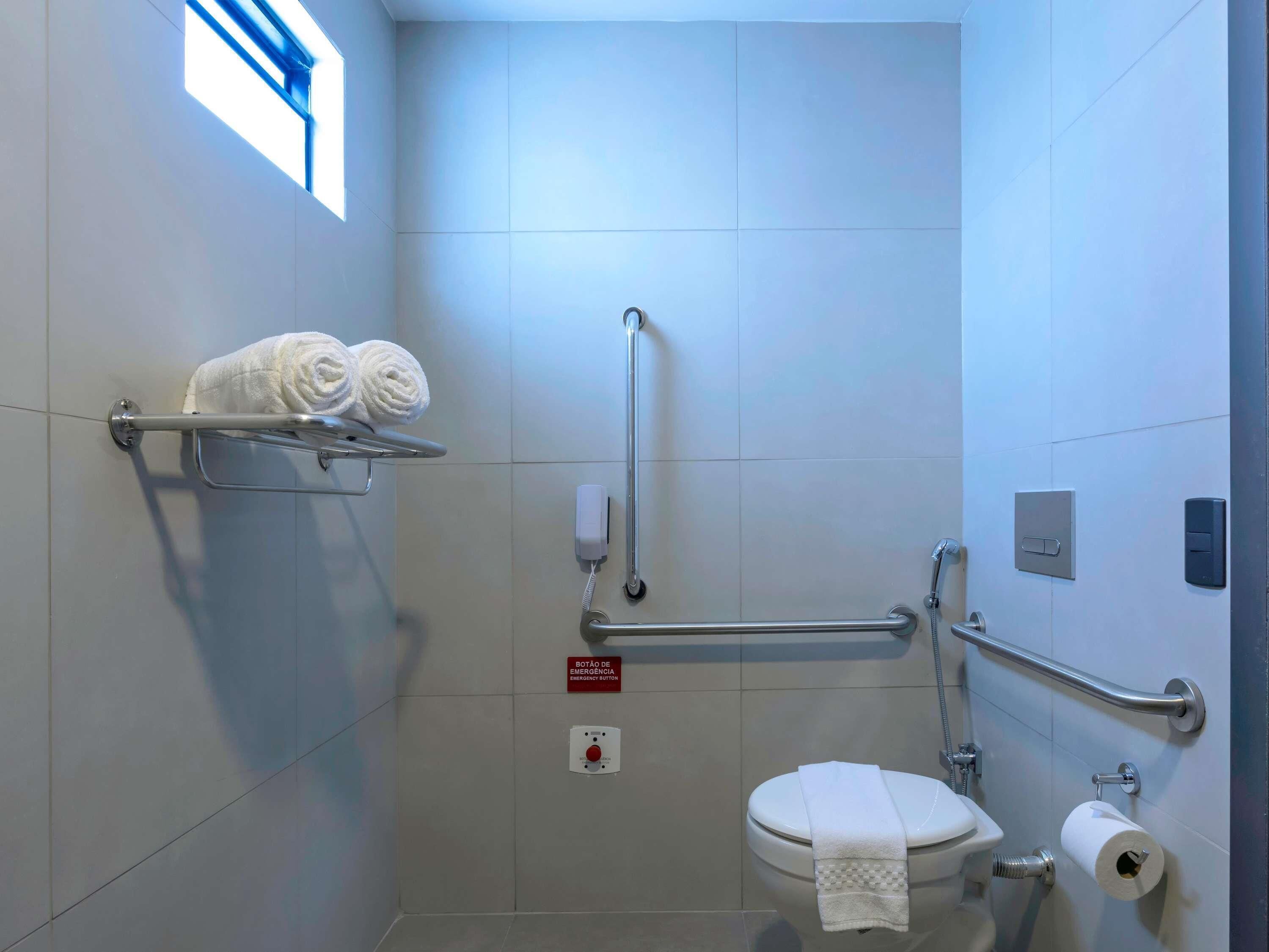 A modern bathroom with a toilet, handrails, a towel rack, and an emergency button.