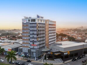 A multi-story building with a prominent 'Smart Fit' sign, a contact number, and a '99' sign on the facade. - Ibis Budget Pindamonhangaba (Pindamonhangaba)