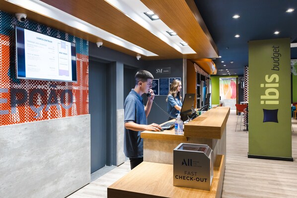 A reception area with a digital display, a 'Fast Check-Out' box, and a 'Budget' sign.