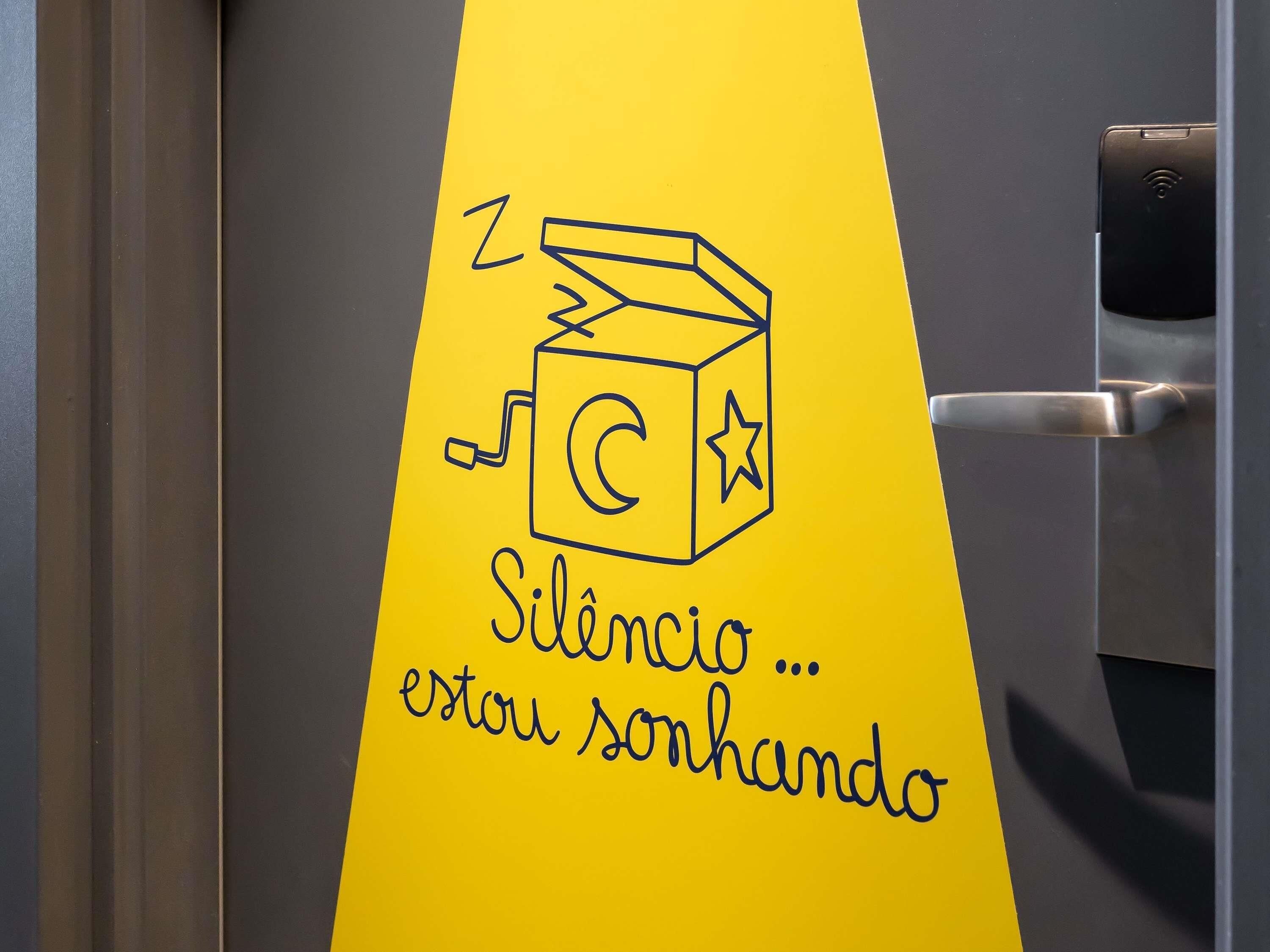 Una puerta con un adhesivo amarillo que muestra un cubo con una estrella y una nota musical, y el texto 'Silêncio ... estou sonhando'.