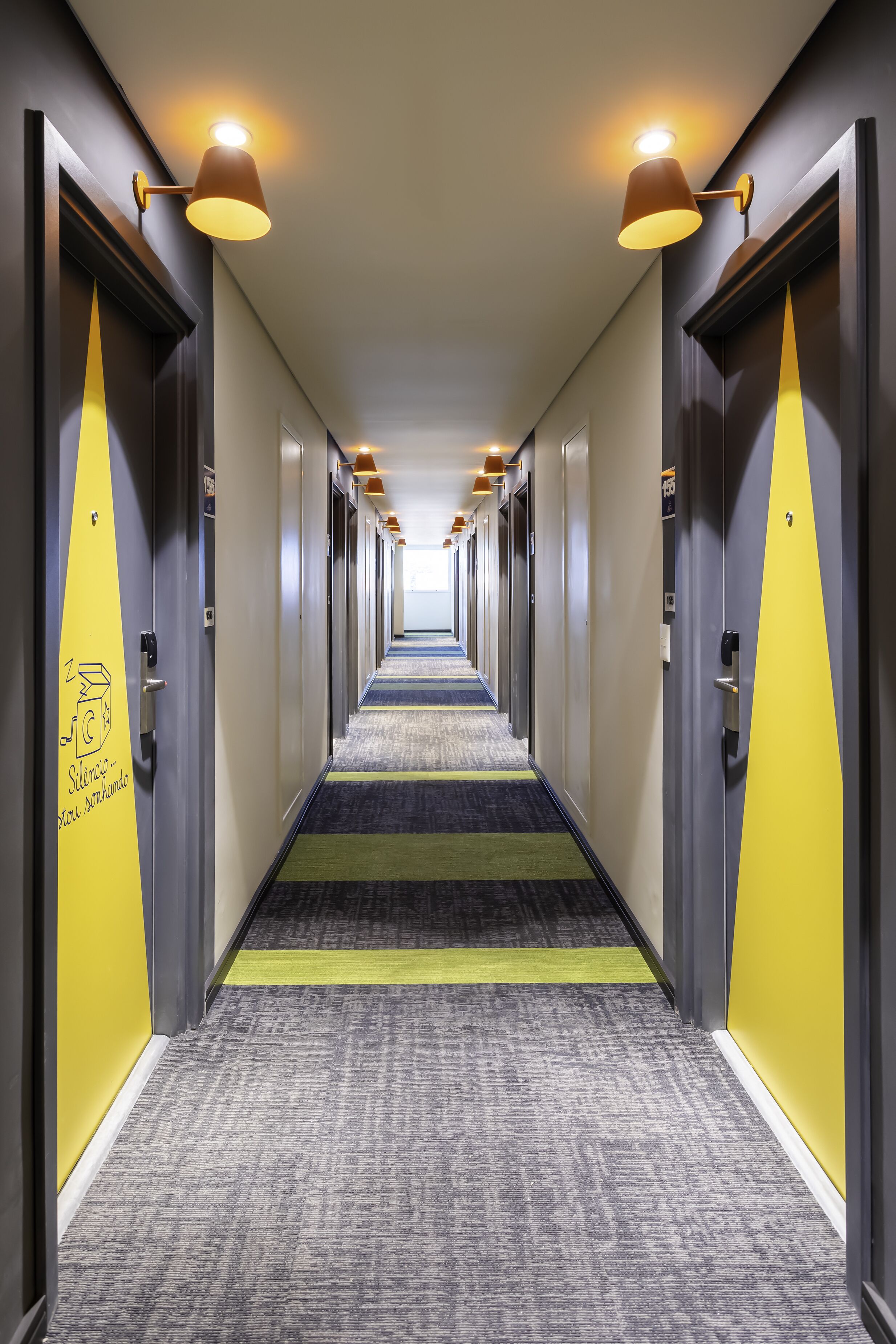 Pasillo de hotel con puertas a ambos lados, pisos alfombrados e iluminación en el techo.