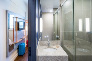 A modern bathroom with a glass shower enclosure, a sink with a marble countertop, and a small mirror above the sink. - Ibis Budget Pindamonhangaba (Pindamonhangaba)