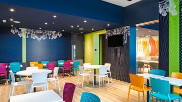 Un comedor moderno con mesas redondas y sillas coloridas, que combina iluminación natural e artificial.