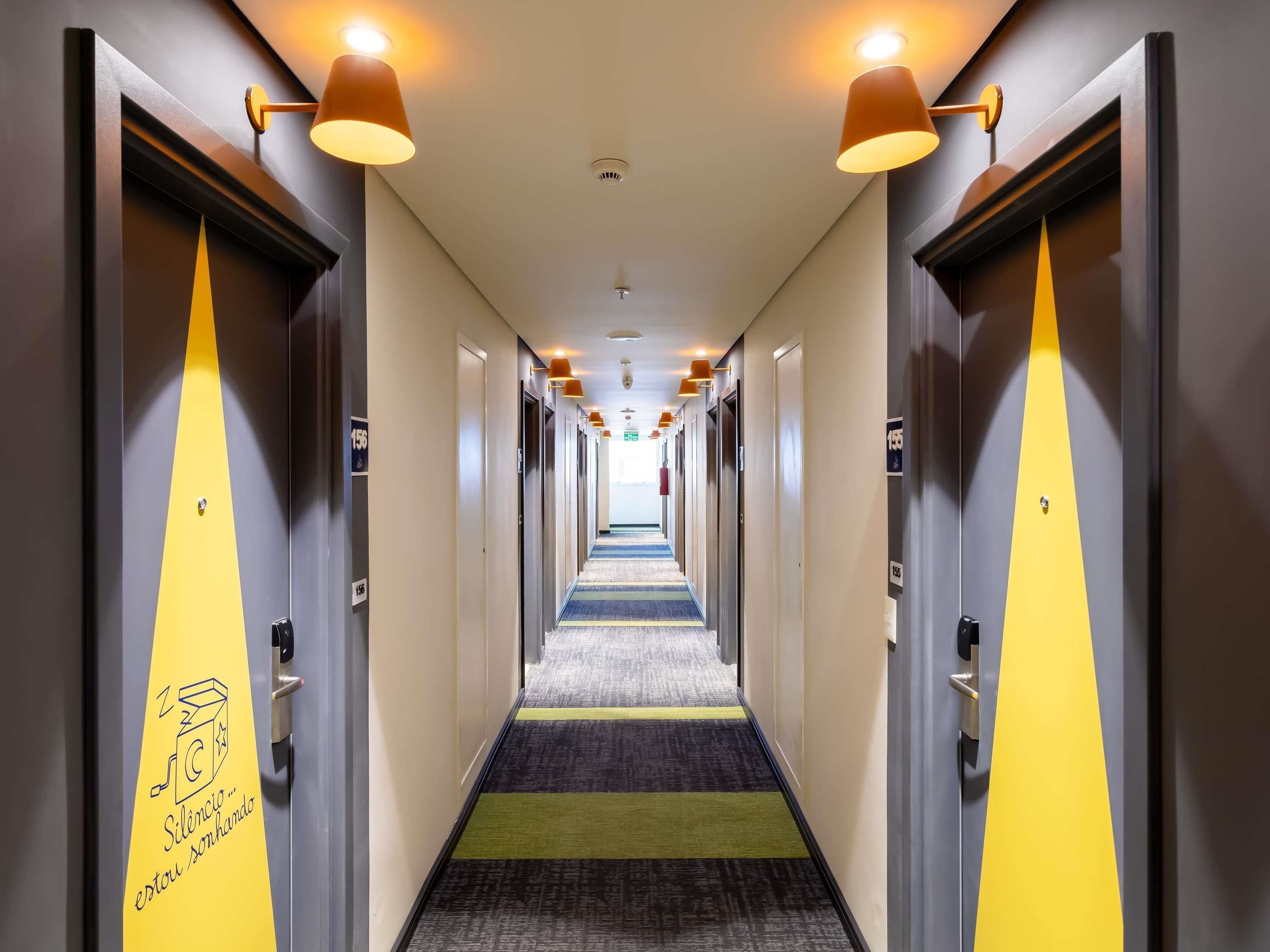 A hotel corridor with doors marked '156', overhead lighting, and a carpeted floor.