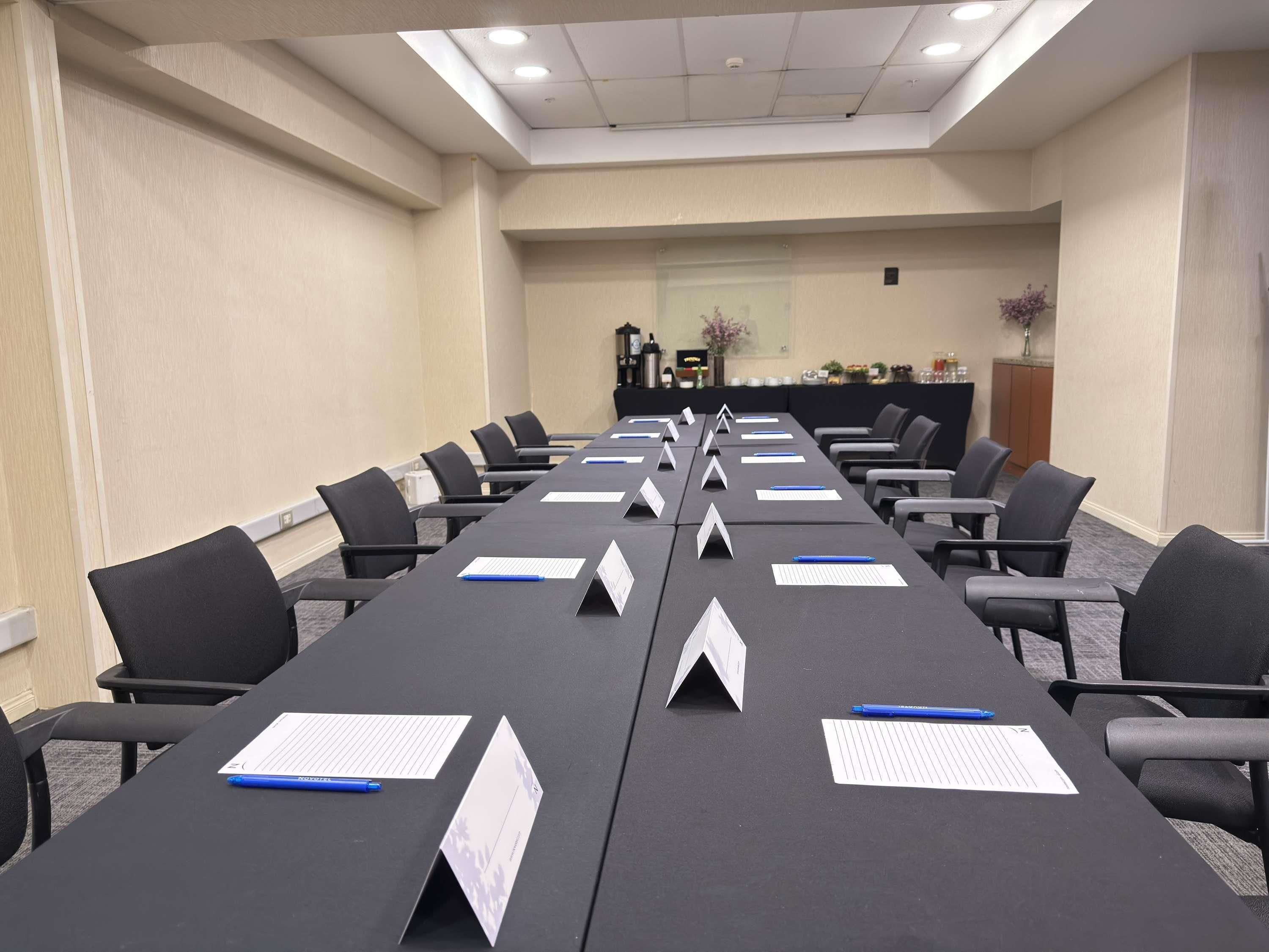 A conference room with a long table, multiple chairs, nameplates, and a podium in the background.