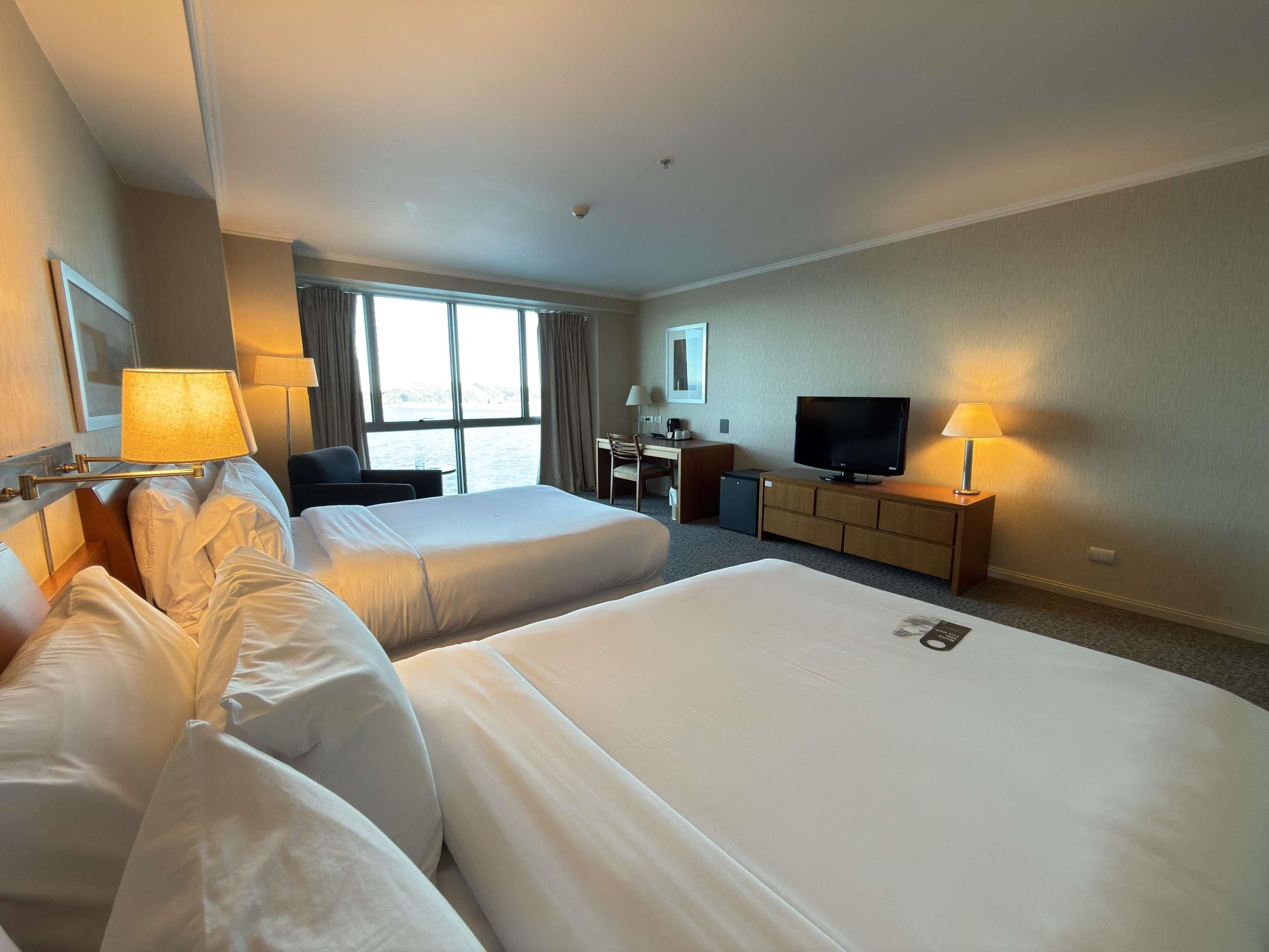 Habitación de hotel con dos camas, un escritorio, televisión y vista al mar.