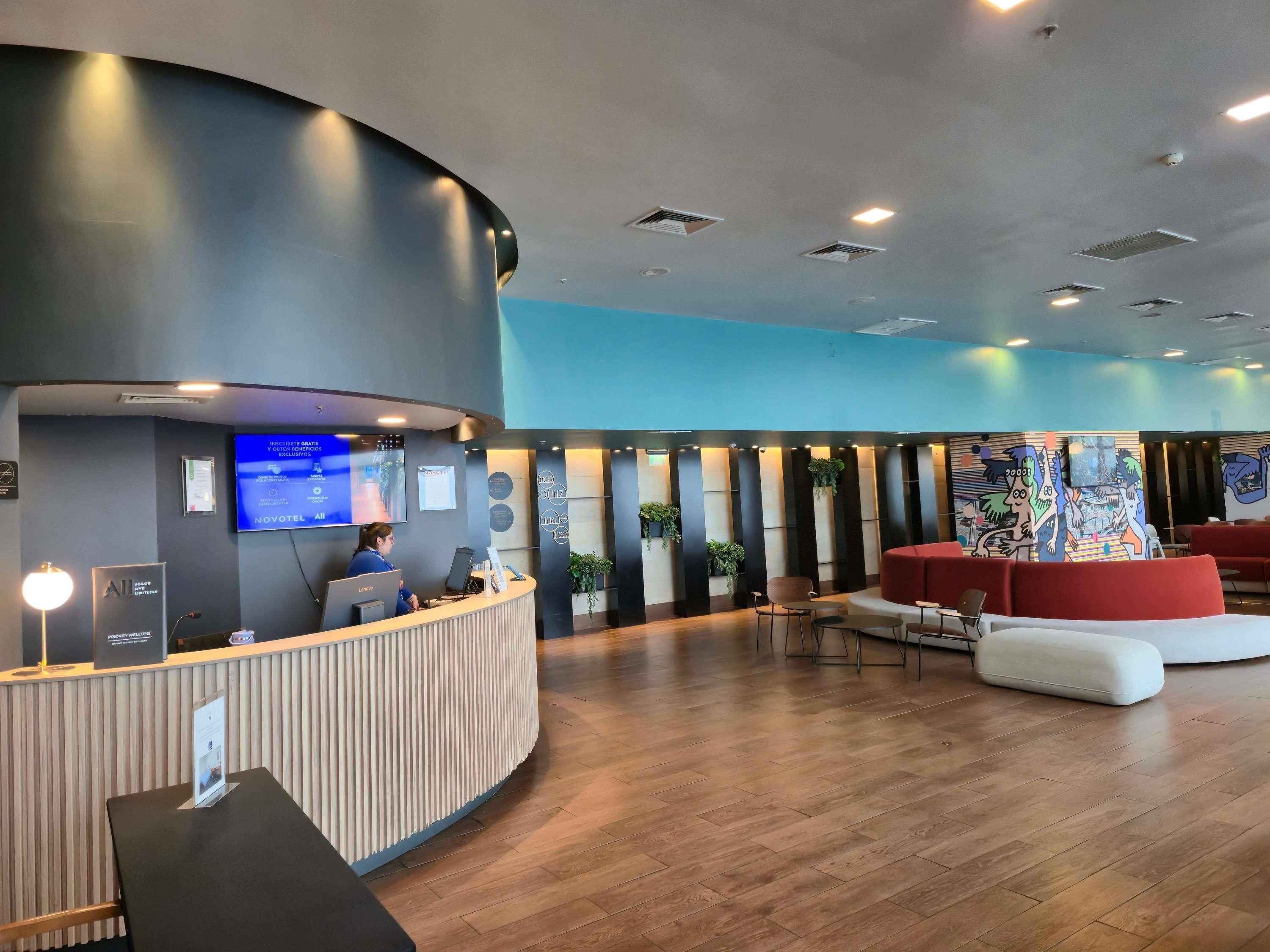 Ein Hotel-Empfangsbereich mit einer gebogenen Rezeption, Sitzgelegenheiten und einem großen, wandmontierten Fernseher.