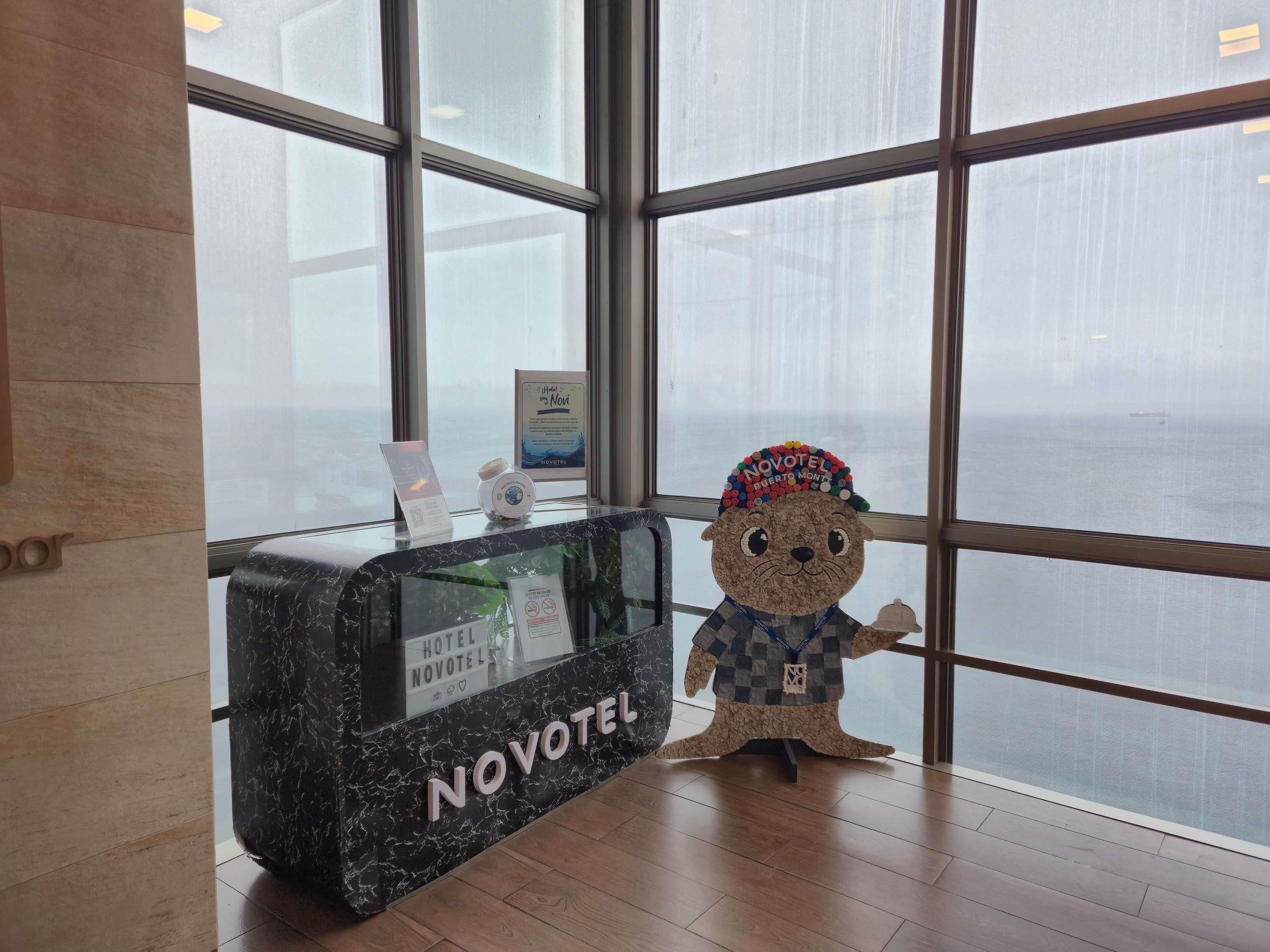 A reception desk with a sign reading 'NOVOTEL' and a plush toy bear with a colorful hat.