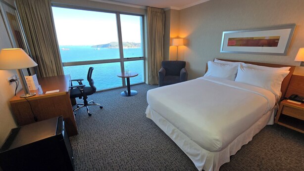A hotel room with a large bed, a desk with a chair, a small table, and a view of the sea. - Novotel Puerto Montt (Puerto Montt)