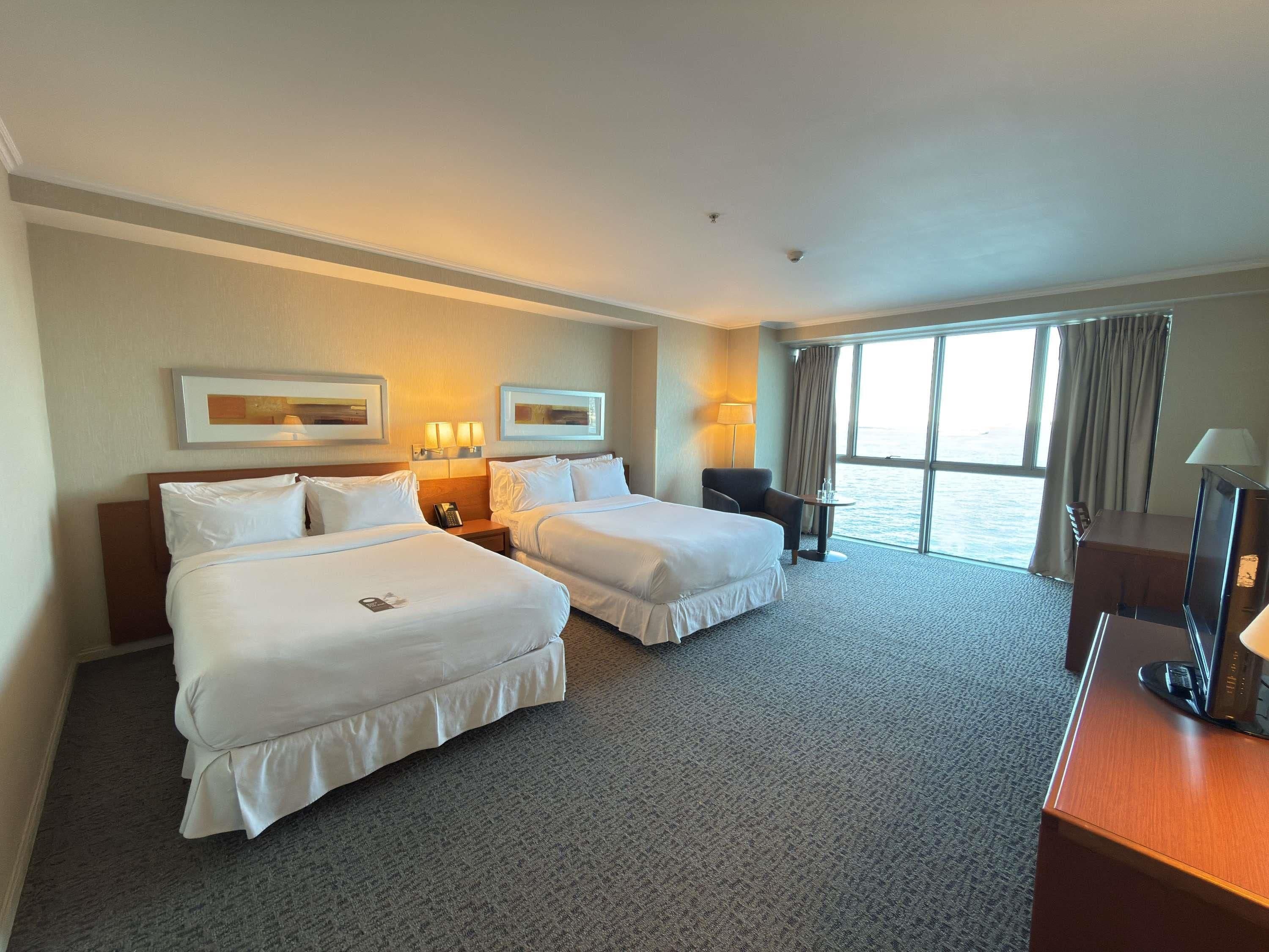 A hotel room with two beds, a desk, a chair, and a large window with curtains.