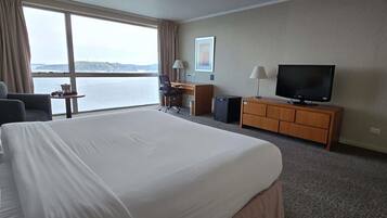 A hotel room with a large bed, a desk with a computer, a television, and a view of the sea.