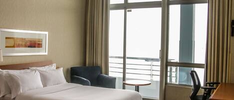 Habitación de hotel con dos camas, una silla, un escritorio y un amplio ventanal con cortinas.