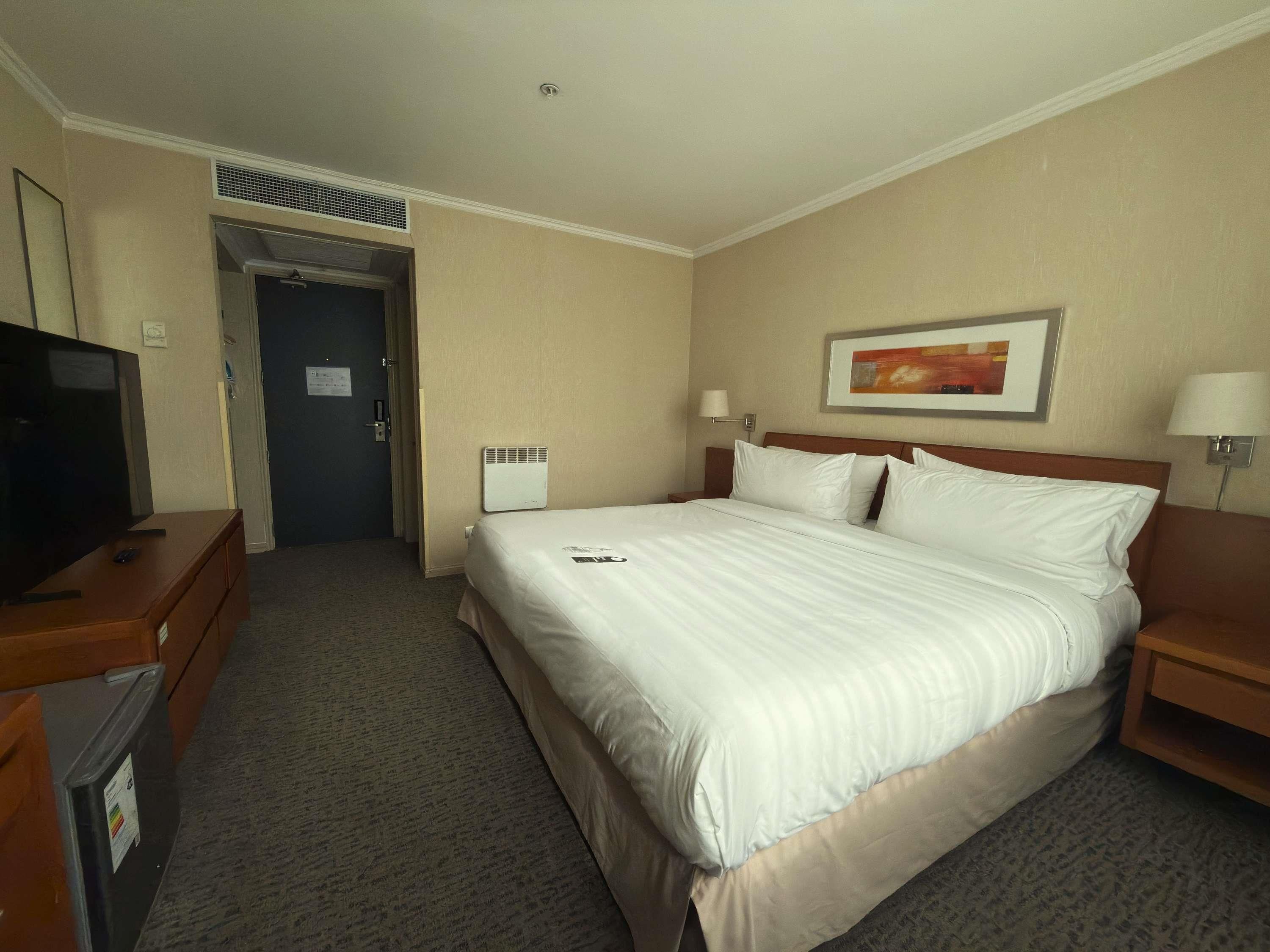 Una habitación de hotel con una cama, un televisor en una cómoda y una pintura en la pared.