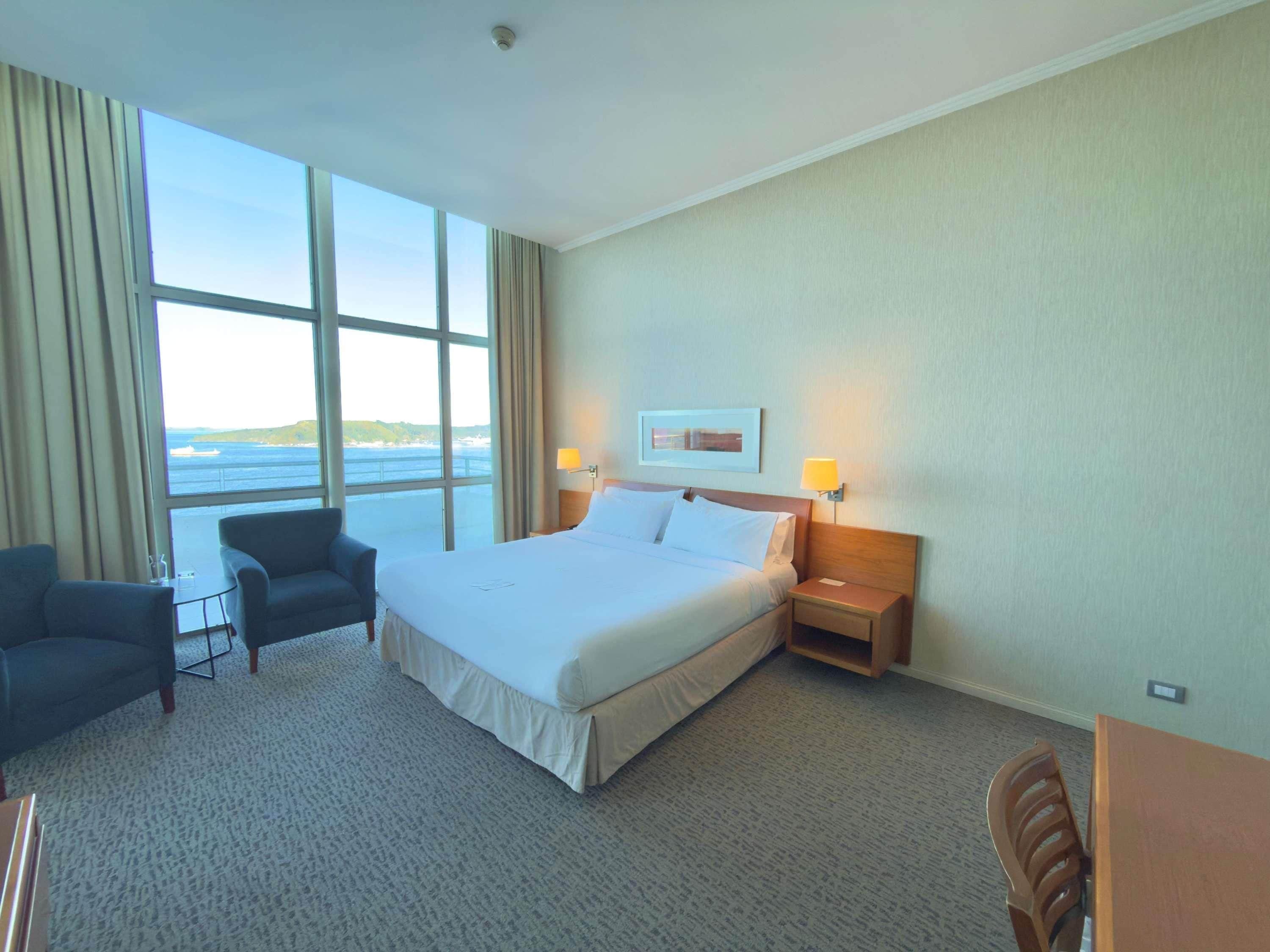 A hotel room with a large bed, two bedside lamps, a desk, and a chair.