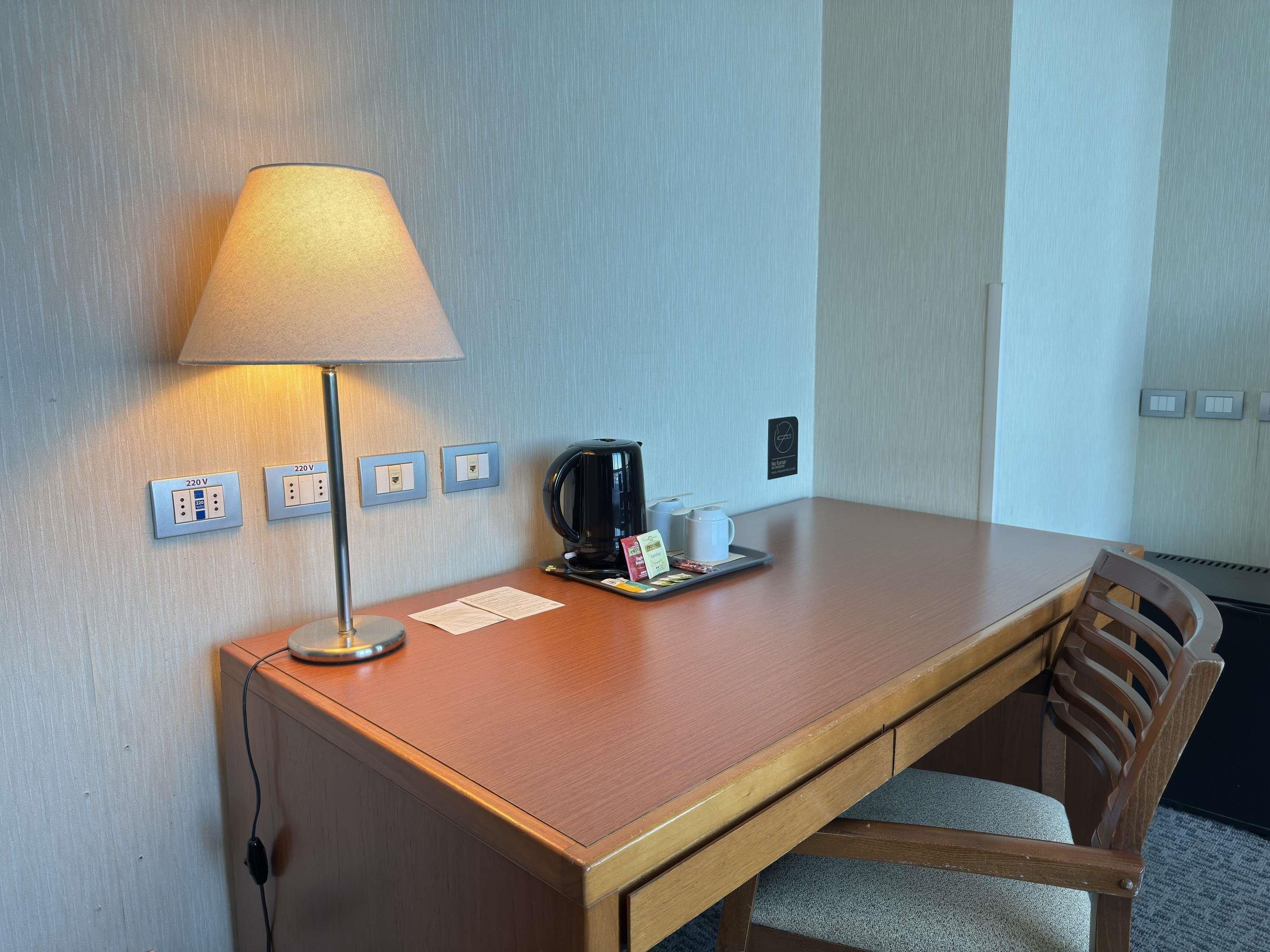 Une chambre d’hôtel avec un bureau en bois, une lampe, une machine à café et un plateau avec une tasse et un menu.