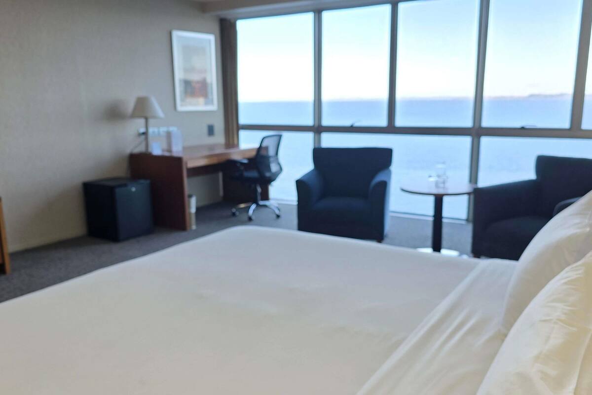Habitación de hotel con una cama grande, un escritorio, dos sillas, una mesita y vista al mar.