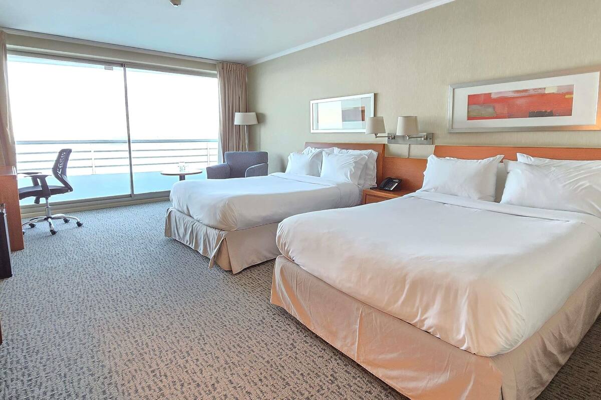 Habitación de hotel con dos camas, un escritorio, una silla, un teléfono y una ventana con vistas.