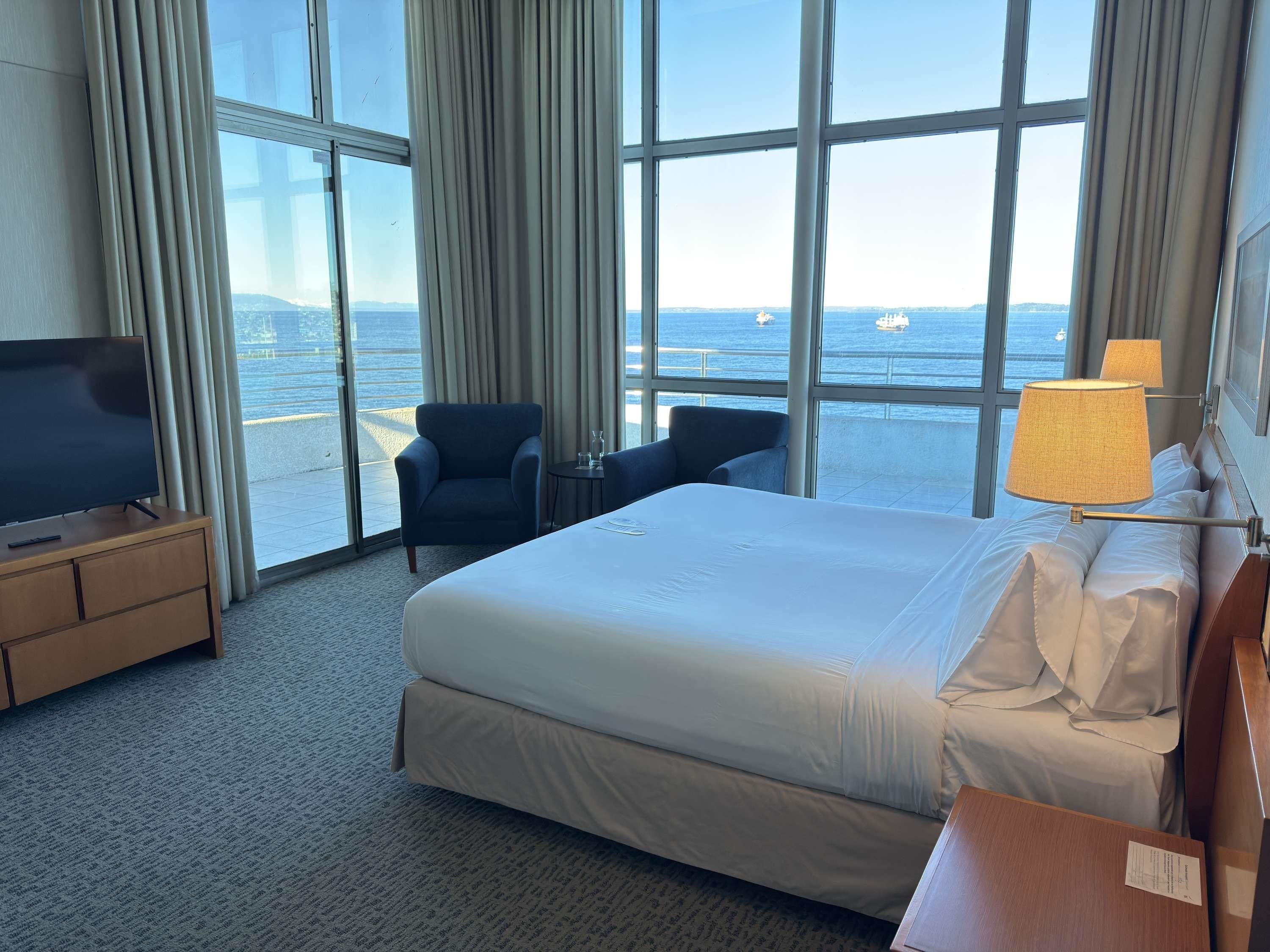 Habitación de hotel con una cama grande, televisión, escritorio, silla y vista al mar.
