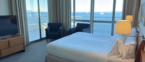 Habitación de hotel con una cama grande, televisión, escritorio, silla y vista al mar.