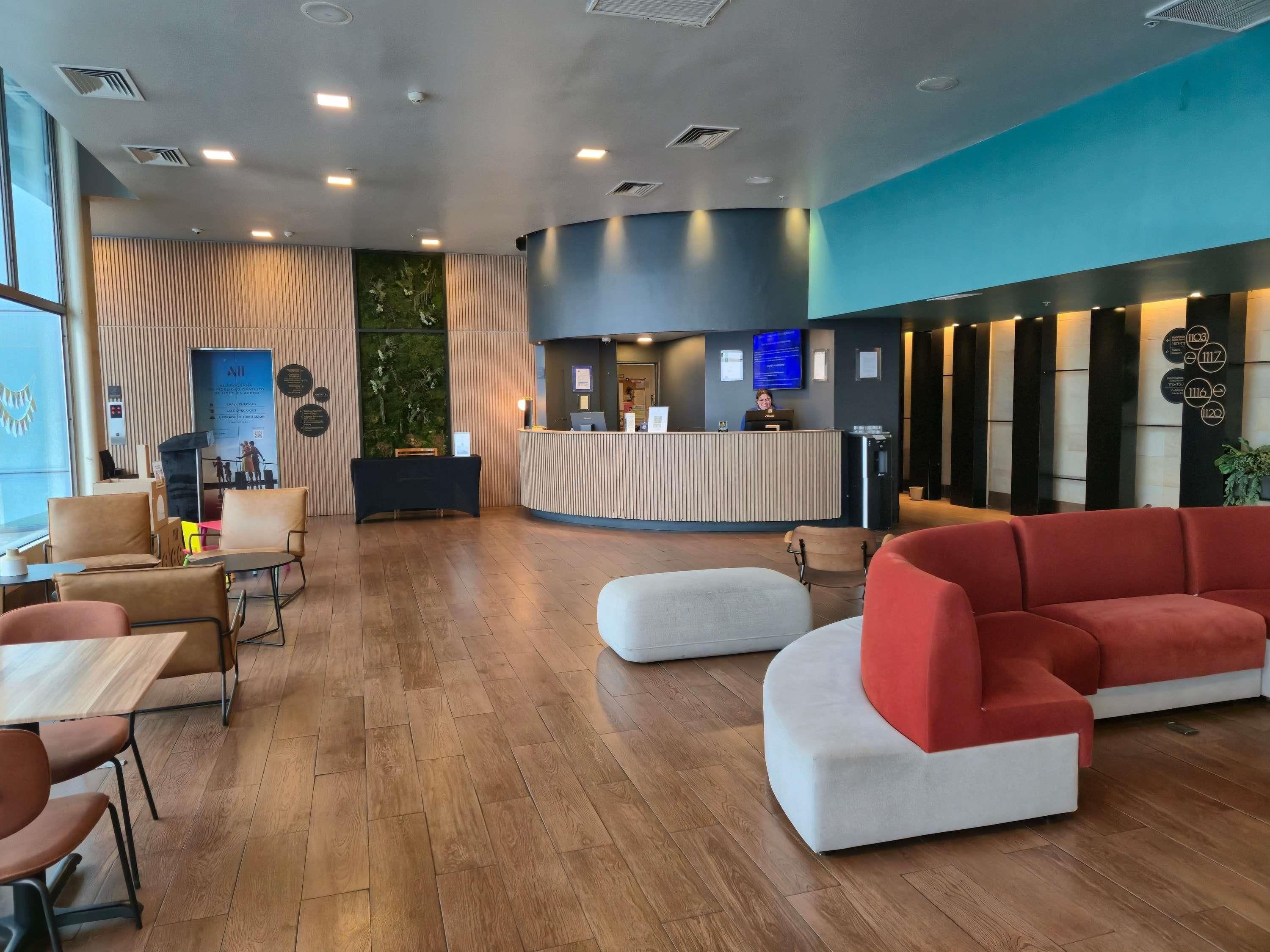 Un vestíbulo de hotel con mostrador de recepción, zonas de estar y suelo de madera.