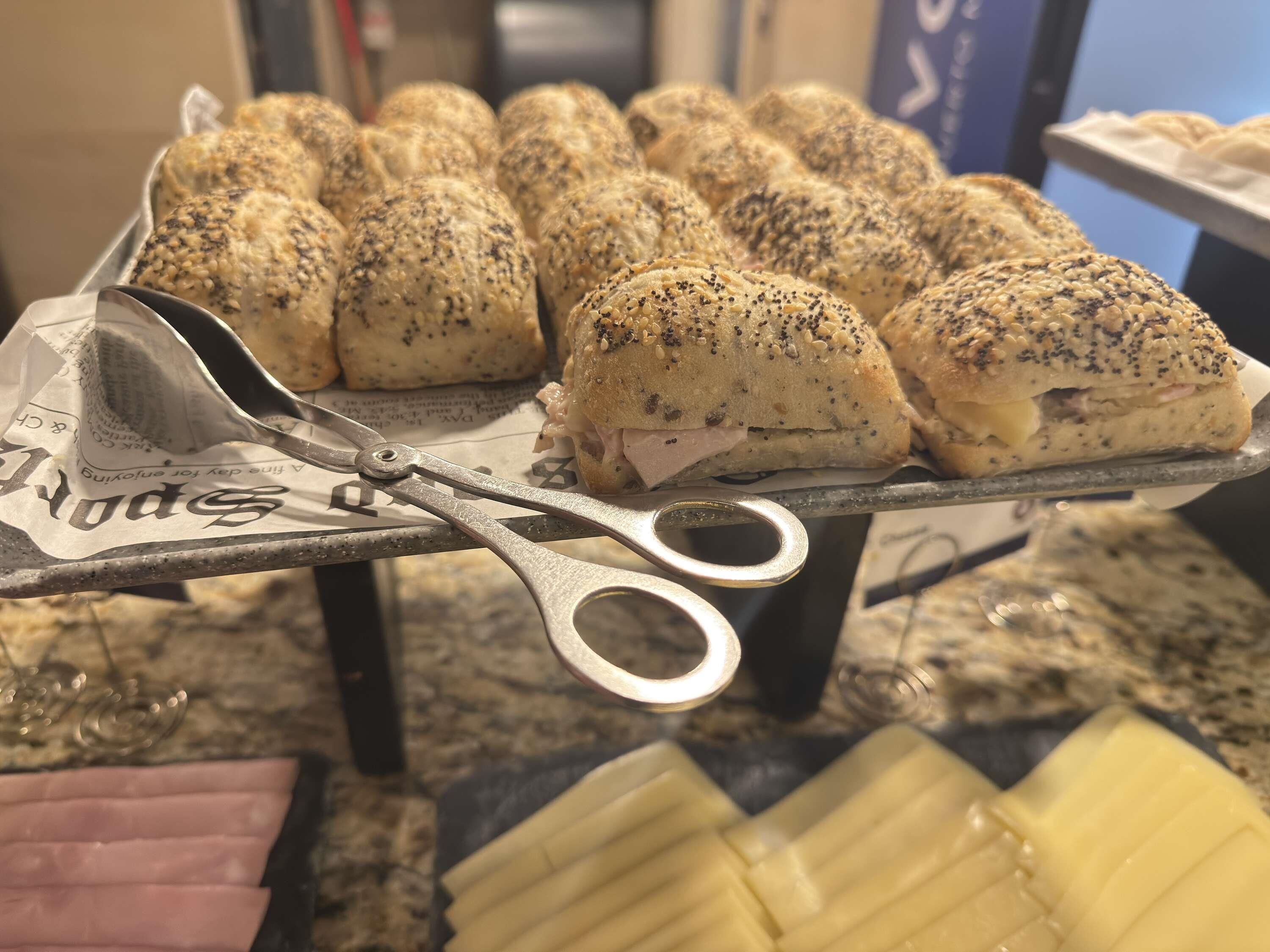 A tray of bread rolls with a metal tongs resting on top, placed on a table with a paper underneath.