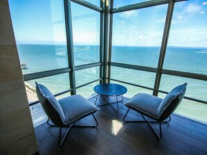 Une pièce dotée d’une grande fenêtre donnant sur la mer, de deux chaises et d’une petite table.