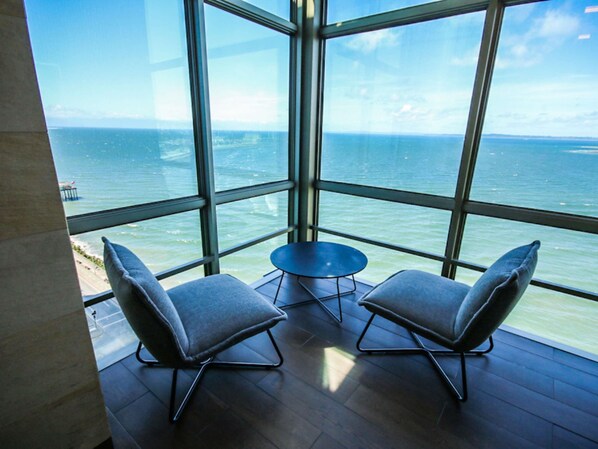 Una habitación con un ventanal grande con vistas al mar, dos sillas y una mesita.