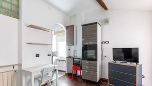 Una cocina compacta con electrodomésticos modernos, un comedor con una silla y un televisor sobre un aparador.