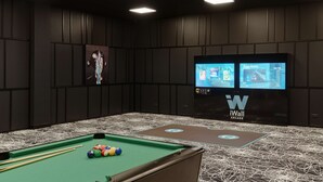 A pool table with balls, a large screen displaying a video game, and a logo on the wall.
