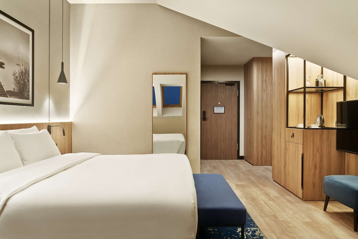 A modern hotel room with a large bed, a desk, a television, and a wardrobe.