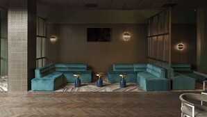 A modern lounge area with a herringbone wood floor, teal upholstered seating, and gold-toned side tables.
