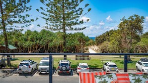 Un espace de stationnement avec plusieurs voitures, un banc et une vue sur la plage et les arbres.