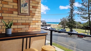 Enjoy the ocean view from this balcony, featuring a framed picture, a potted plant, and two stools.