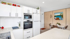 Une cuisine moderne avec des meubles blancs, un four à micro-ondes, un four et un réfrigérateur. On y trouve également un coin repas avec une table et des chaises, ainsi qu’un tableau accroché au mur.