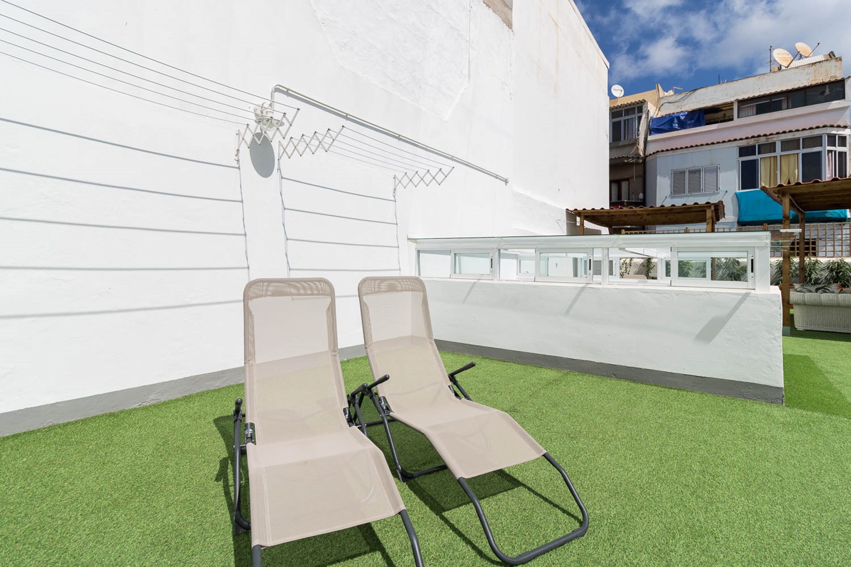 Two sun loungers on artificial grass with a white wall and a building in the background.
