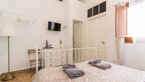 Een slaapkamer met een bed, nachtkastje, lamp, televisie en een kledingkast.