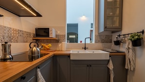 Een moderne keuken met een houten aanrecht, een roestvrijstalen waterkoker, een magnetron en een raam met uitzicht op een gebouw.