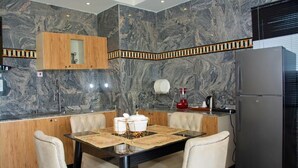 A modern kitchen with marble walls, a wooden cabinet, a refrigerator, and a dining table with chairs. - St Jacobs Hotel (Akure)