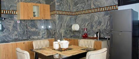 Une cuisine moderne avec des murs en marbre, un meuble en bois, un réfrigérateur et une table à manger avec des chaises.