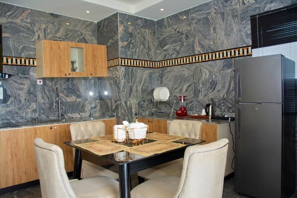 A modern kitchen with marble walls, a wooden cabinet, a refrigerator, and a dining table with chairs.