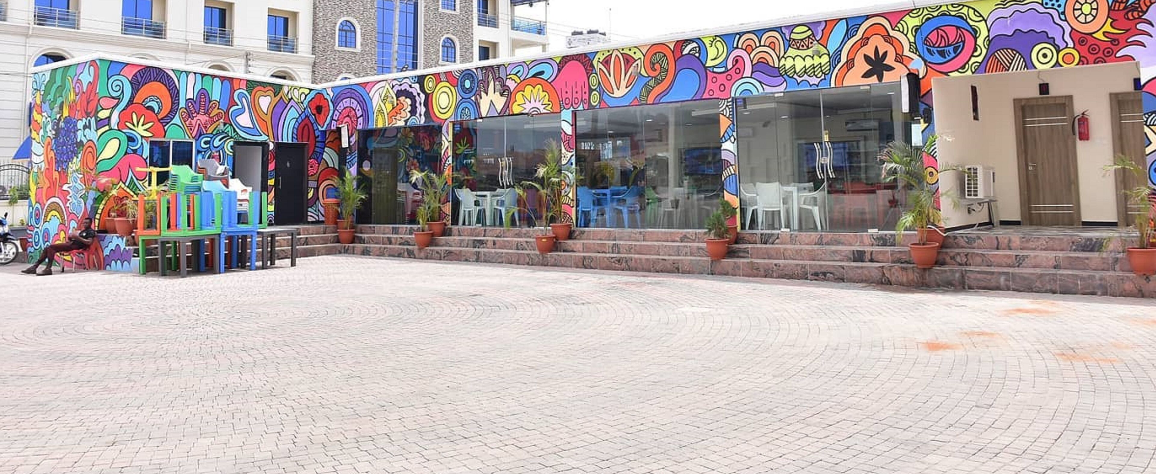 A colorful building with a vibrant mural on the exterior, outdoor seating area with chairs and tables, and potted plants.