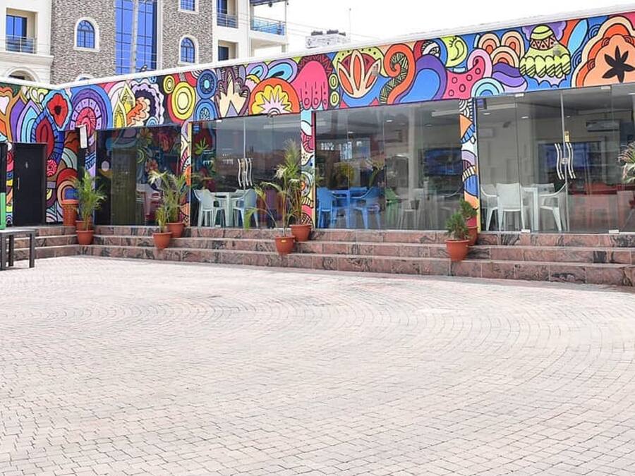 A colorful building with a vibrant mural on the exterior, outdoor seating area with chairs and tables, and potted plants.