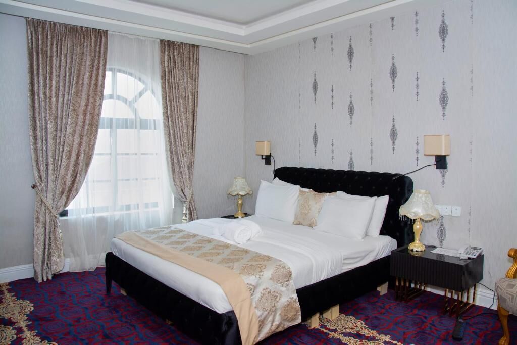 Habitación de hotel con una cama grande, dos mesitas de noche con lámparas, una ventana con cortinas y un papel tapiz estampado.