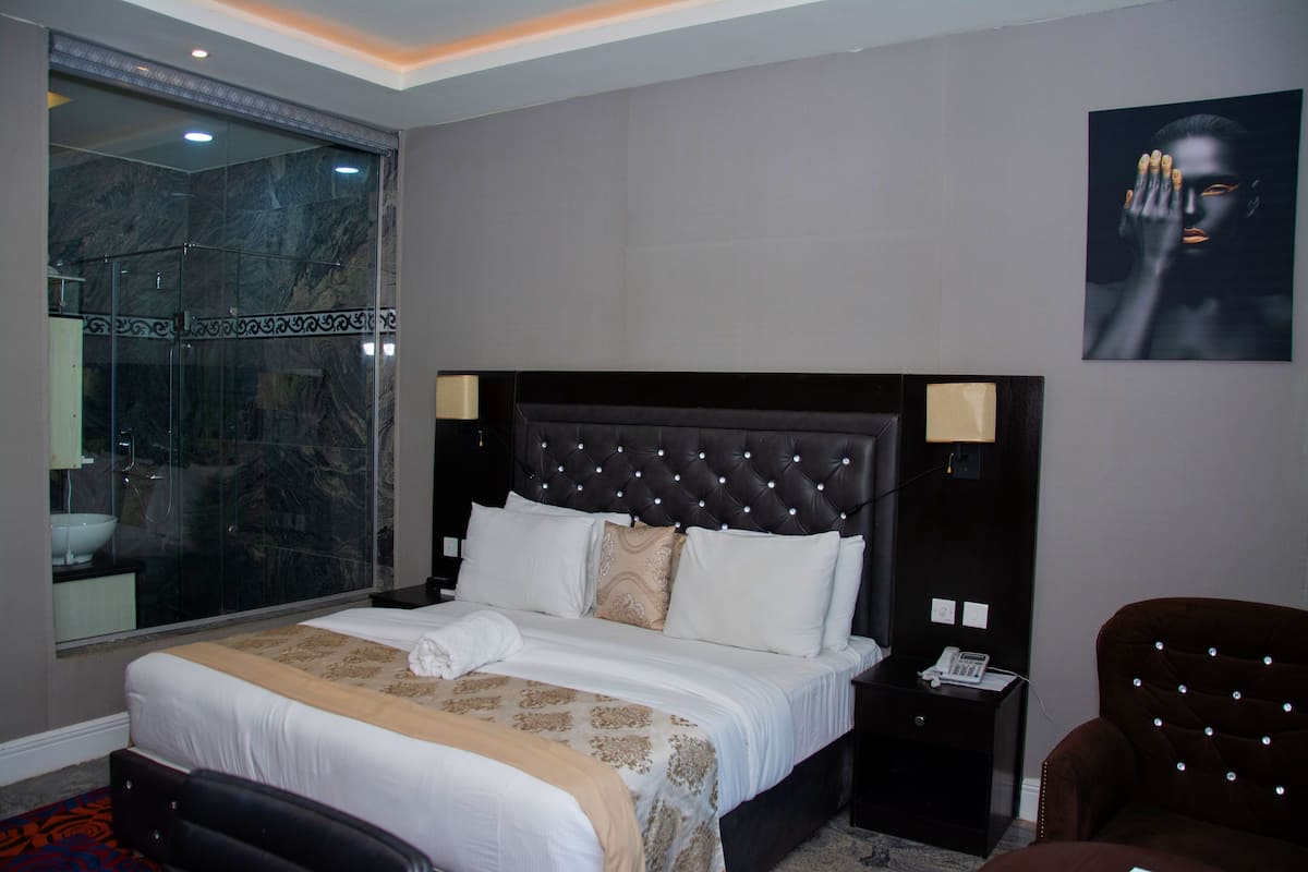 Habitación de hotel con una cama grande, cabina de ducha de vidrio, mesita de noche con lámpara y una obra de arte colgada en la pared.