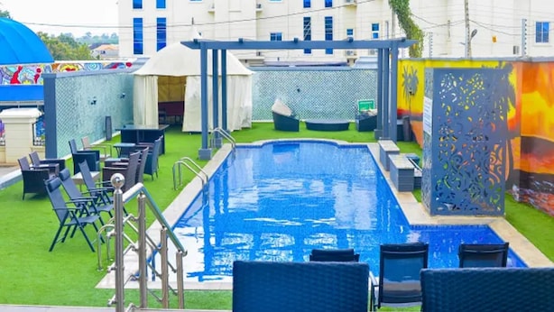 A swimming pool with lounge chairs and a covered seating area, surrounded by a fence and a building in the background. - St Jacobs Hotel (Akure)