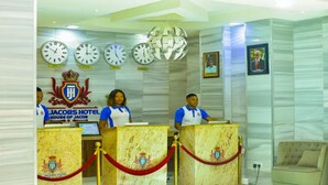 A reception area with a marble counter, clocks, and a coat of arms emblem. - St Jacobs Hotel (Akure)