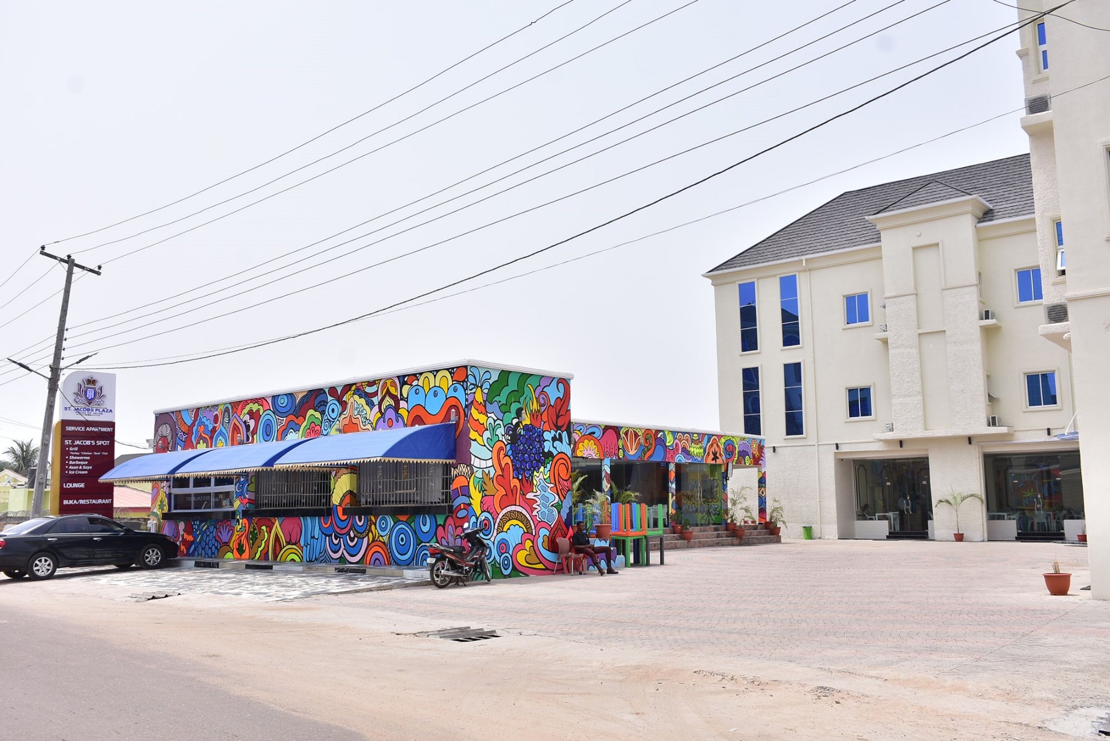 A colorful building with a mural, a parked motorcycle, and a car in front.