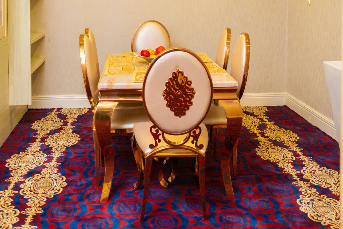 Comedor con una mesa dispuesta para cuatro personas, rodeada de sillas ornamentales con detalles dorados.