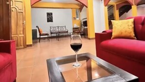 Un vaste espace de vie avec un canapé rouge, une table basse en verre sur laquelle repose un verre à vin, et, au fond, une vue sur un coin repas.